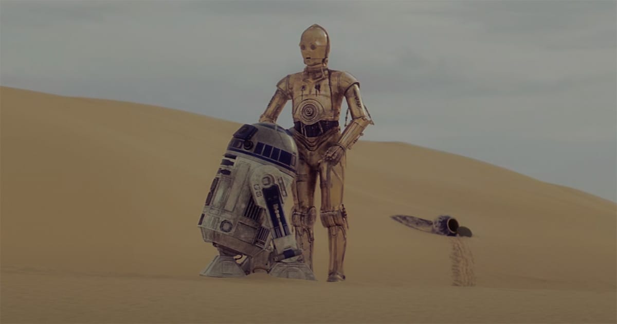 R2-D2 and C-3PO stand together in a desert landscape on Tatooine, with a crashed escape pod behind them in a scene from "Star Wars."