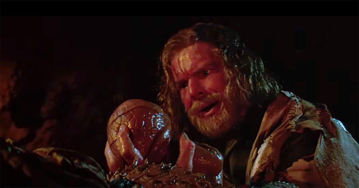 Davidge holding Shigan’s newborn child, Zammis, illustrating the film’s themes of empathy, transformation, and shared responsibility in Enemy Mine (1985)