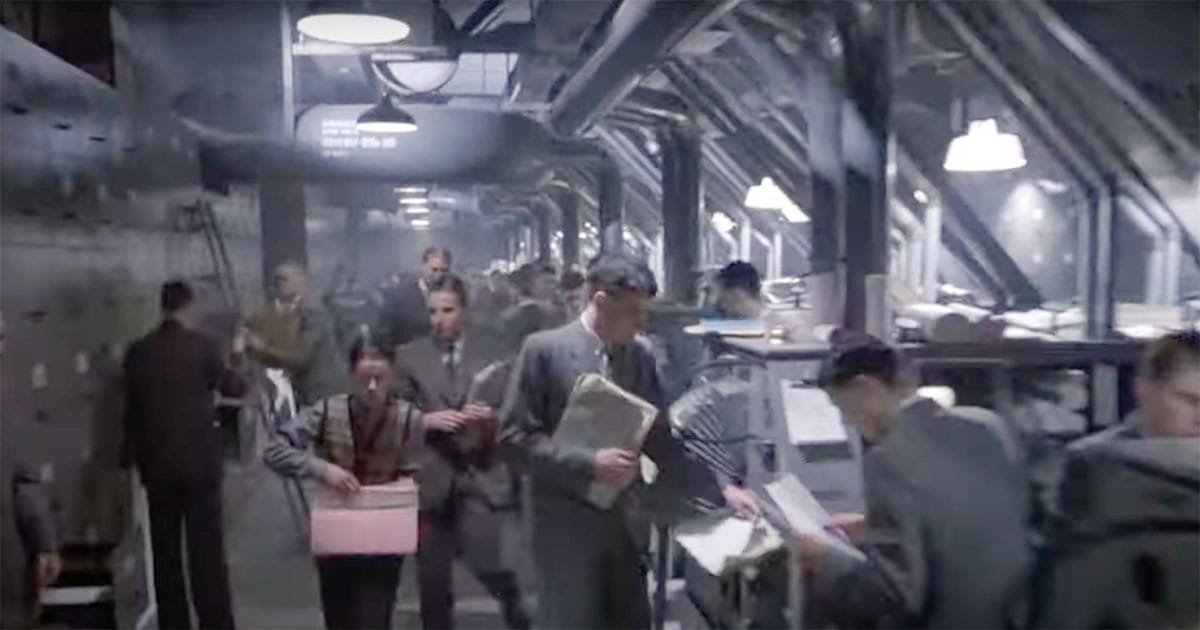 A wide corridor packed with office workers carrying folders beneath looming ductwork and harsh lighting, capturing the scale and absurdity of bureaucracy in Terry Gilliam’s "Brazil" (1985).