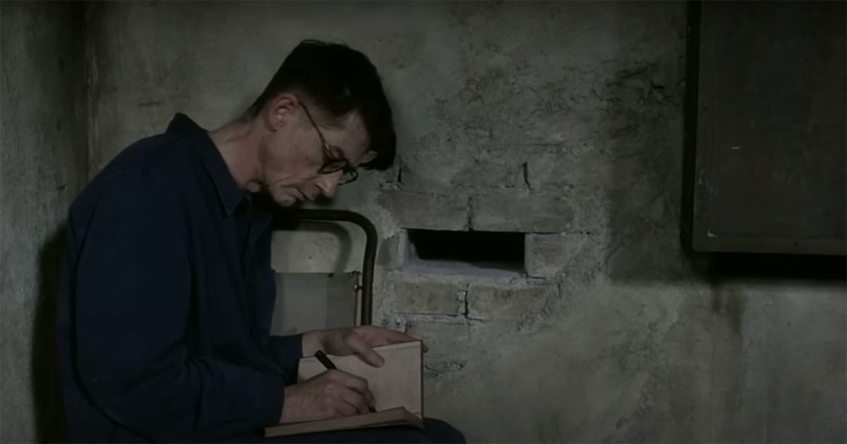 John Hurt as Winston Smith writing in a secret journal in a dimly lit corner in the 1984 film Nineteen Eighty-Four.