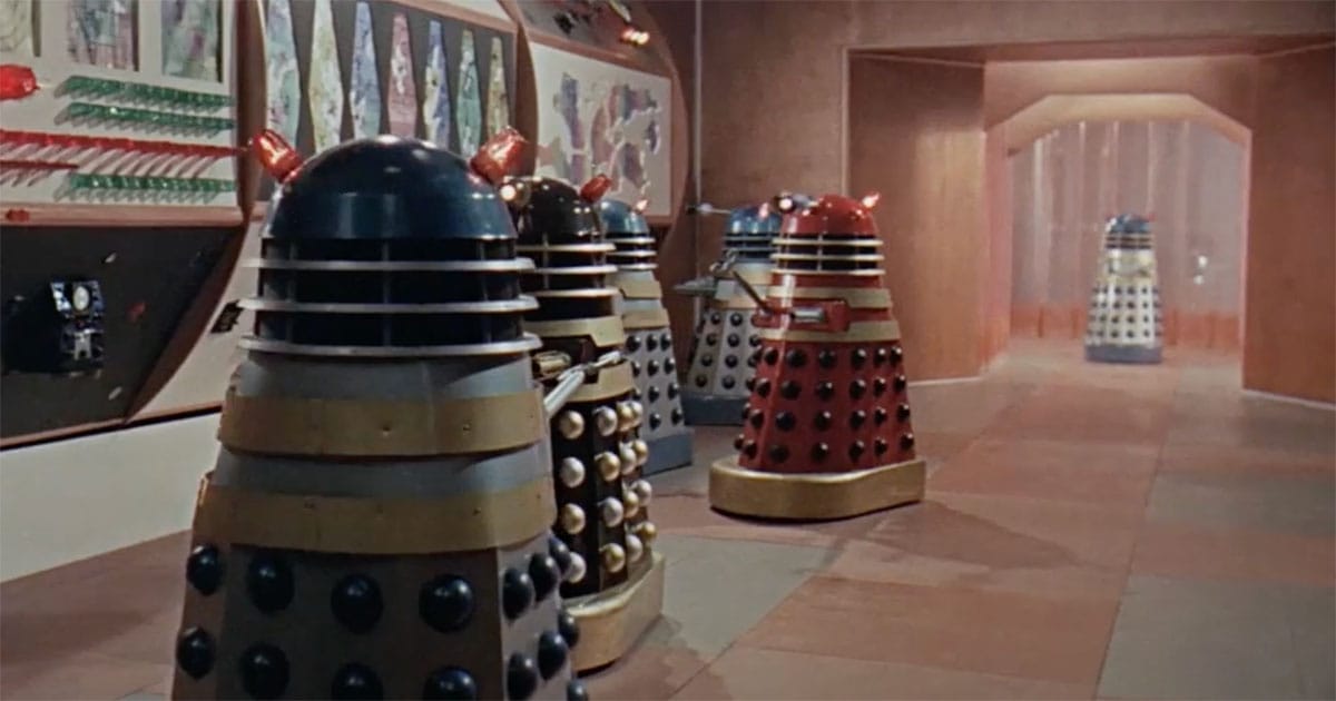 A group of colorful Daleks from a classic Doctor Who scene assembled in a futuristic control room