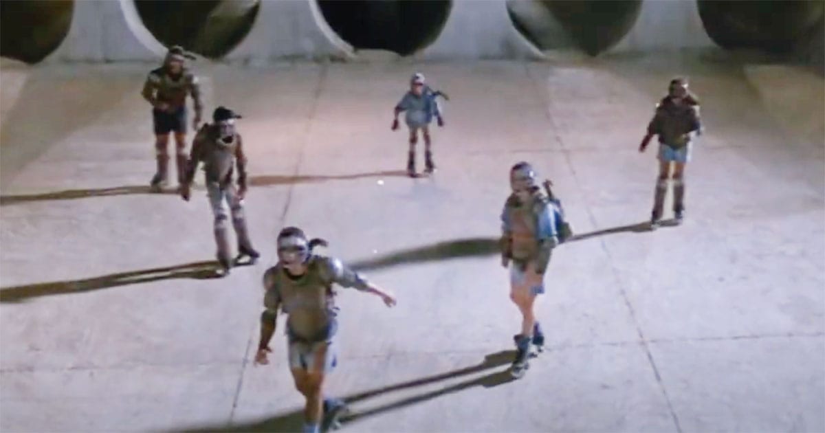 Wide shot of teenagers in sci-fi gear on roller skates standing before massive tunnels in Solarbabies.