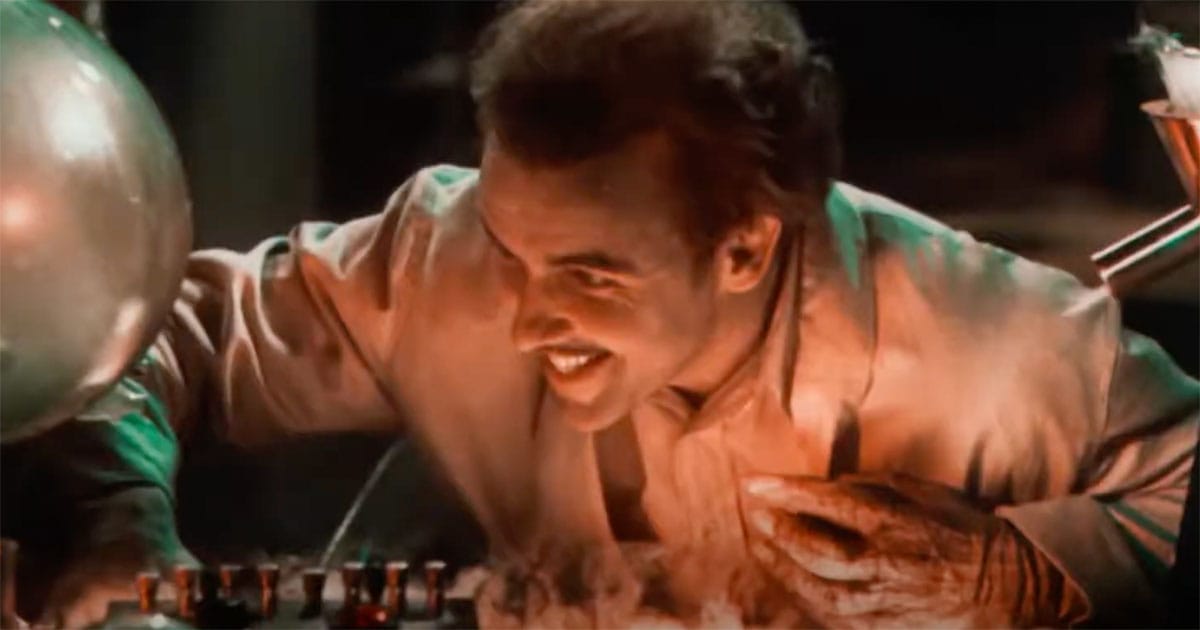 Smiling mad scientist lit by red and green light in "Doctor X" (1932) operating lab equipment in two-strip Technicolor.