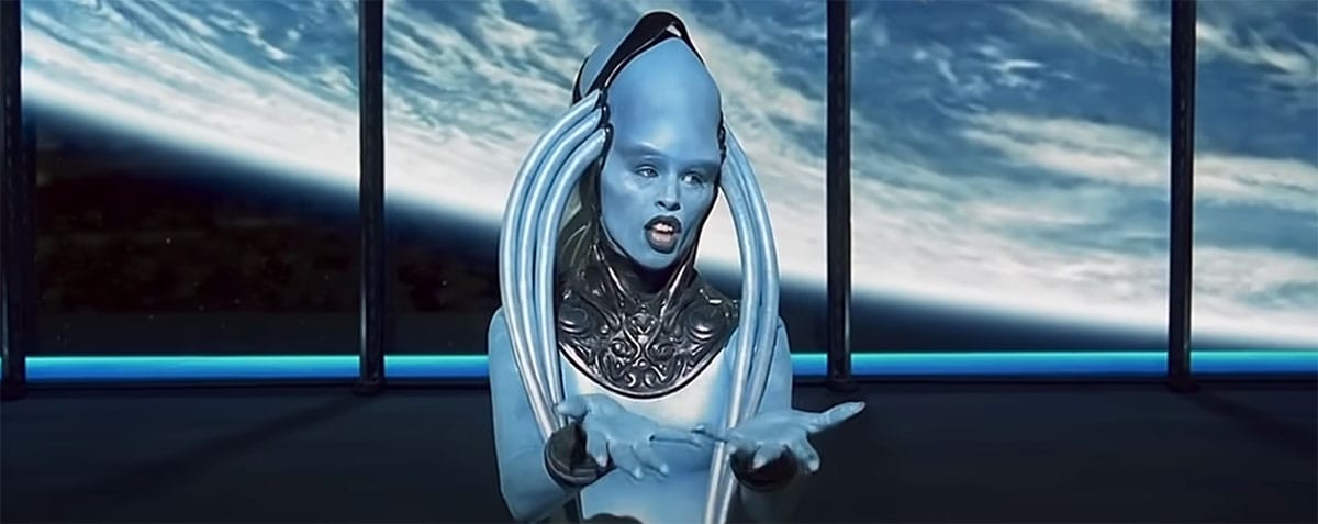 The Diva Plavalaguna sings with a fiery celestial body behind her, hands raised in dramatic expression during her performance in "The Fifth Element."