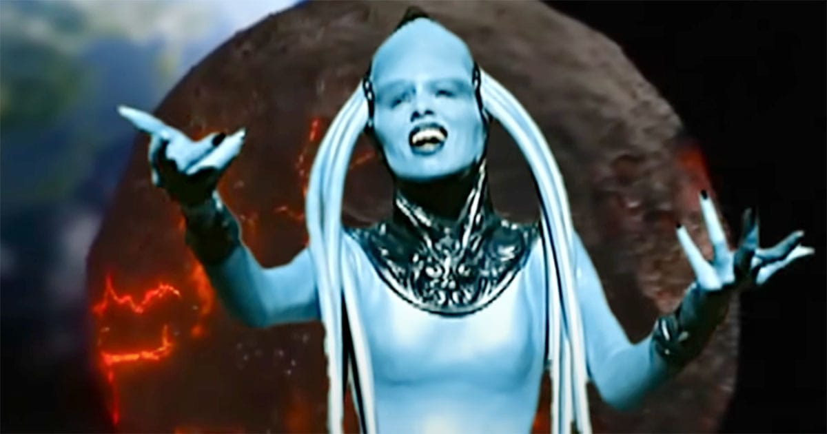 The Diva Plavalaguna sings with a fiery planetary object behind her, arms open in a gesture of expression during her performance in "The Fifth Element."