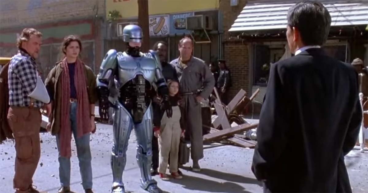RoboCop surrounded by civilians on a Detroit street in the 1987 film "RoboCop," symbolizing his role as both enforcer and guardian in a fractured society.