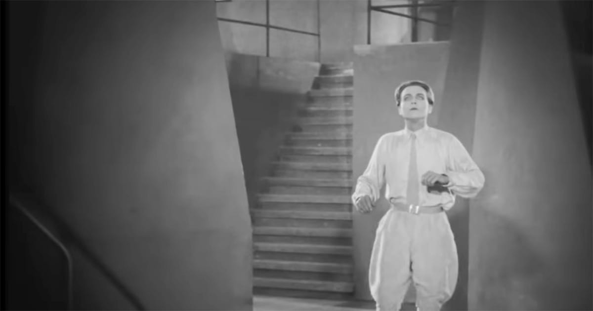 Freder from Metropolis (1927) standing in a stark stairwell, looking upward in awe, symbolizing a journey of discovery through the film’s layered world.
