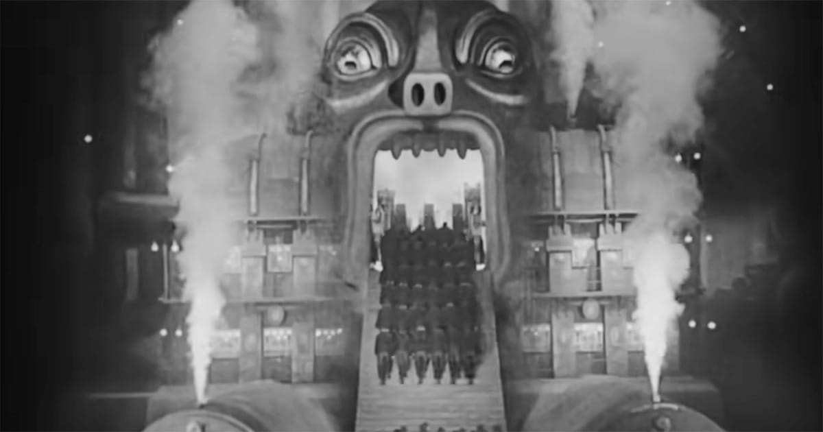 Scene from Metropolis (1927) showing workers in uniform marching into a giant industrial machine with a monstrous face, symbolizing the sacrifice of labor.