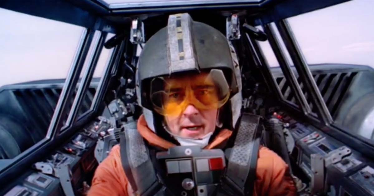 Star Wars scene showing Rebel pilot Wedge Antilles in cockpit wearing orange flight suit and helmet, a memorable background character from the original trilogy.