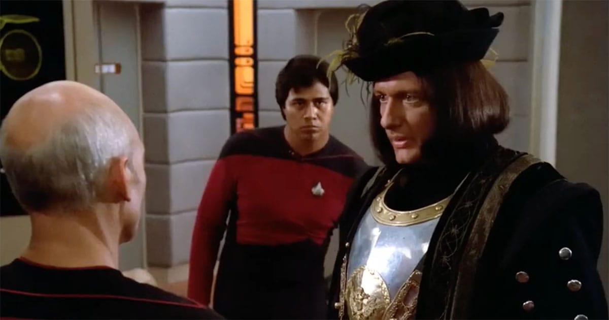 Q wearing a Renaissance-style outfit with armor and a feathered hat confronts Captain Picard in Star Trek: The Next Generation episode “Encounter at Farpoint.”