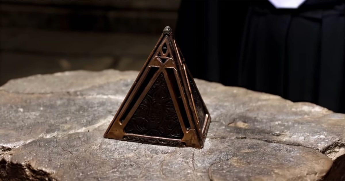 Bronze triangular holocron sitting on a rough stone surface in a dimly lit chamber.