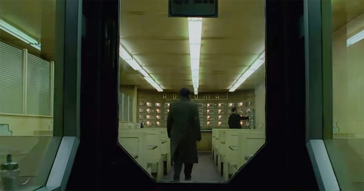 A man walks through a diner doorway under harsh fluorescent light in a scene from “Dark City.”