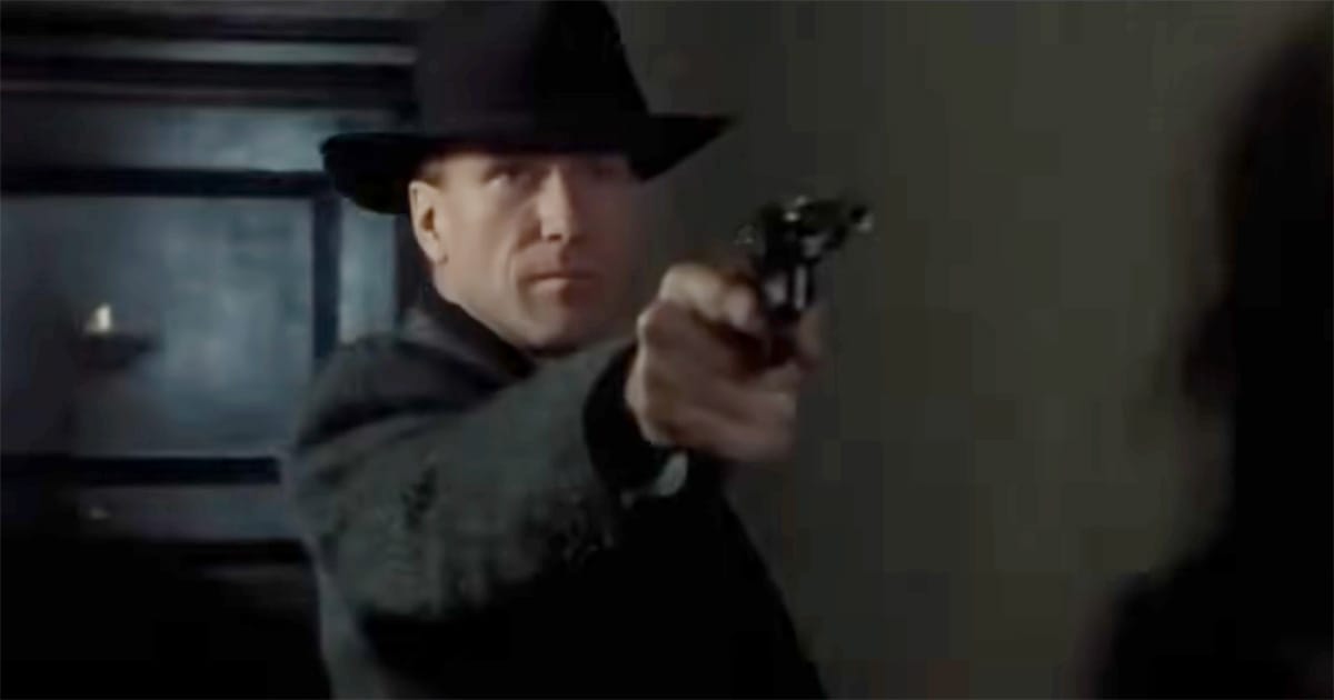 A man in a dark coat and hat points a revolver in the shadows, his face tense with resolve, from “Dark City.”