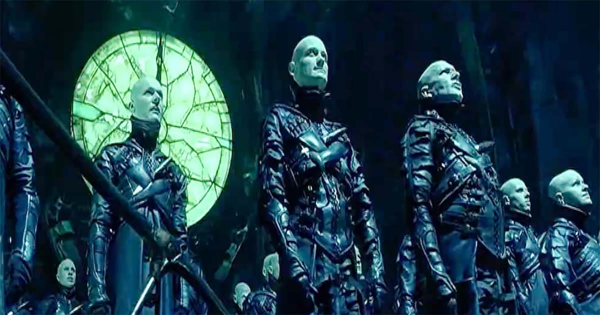 The pale Strangers stand beneath a glowing green light, their black coats gleaming in the shadows, from “Dark City.”