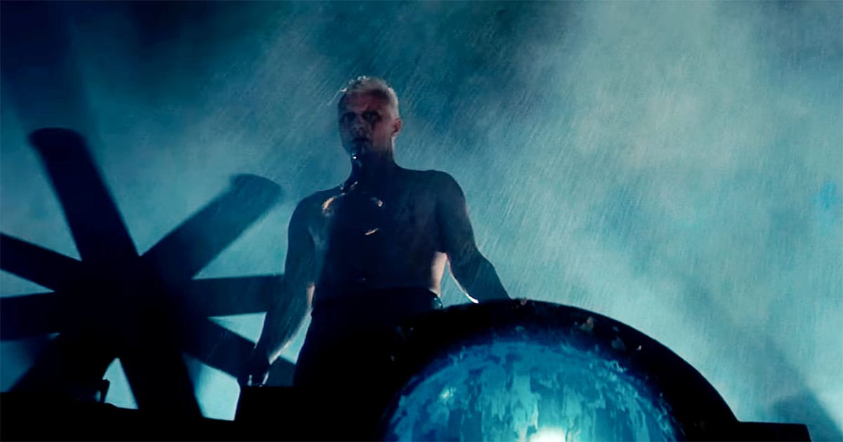 Man standing shirtless in heavy rain on a rooftop.