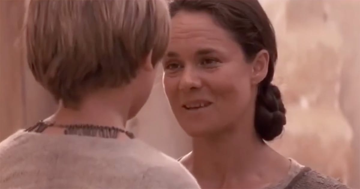 Shmi Skywalker looking at young Anakin with a serious, thoughtful expression outside their home on Tatooine.