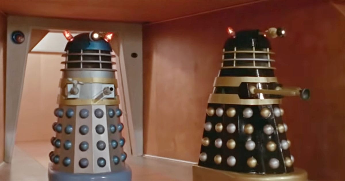 Two Daleks positioned in a narrow corridor in the 1965 film Doctor Who and the Daleks, shown as rigid enclosed machines.