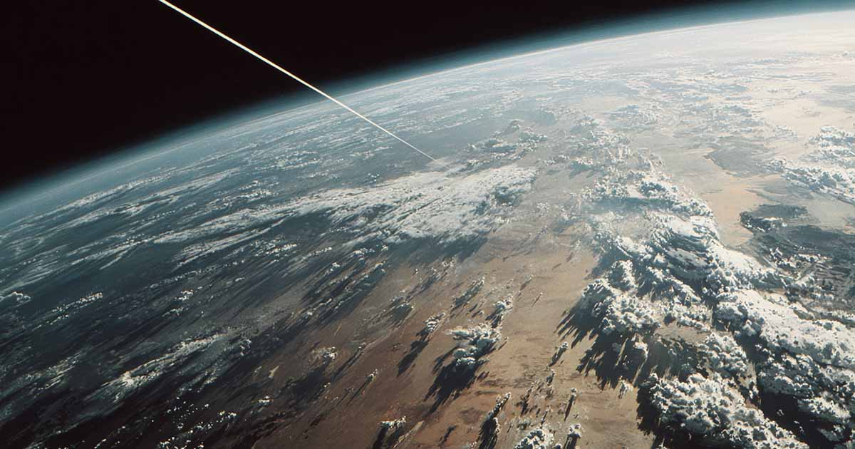 View of Earth from orbit with a thin space elevator cable descending toward the planet, clouds and weather systems visible below.