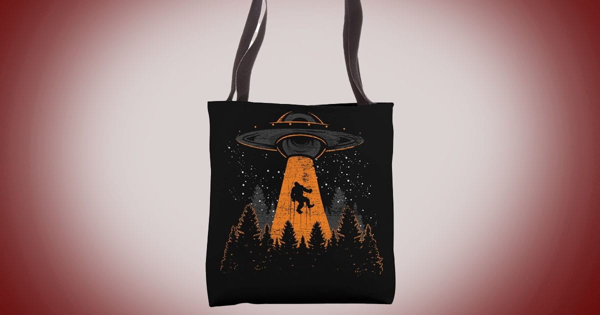 Science fiction tote bag with UFO abducting Bigfoot illustration above forest silhouette.