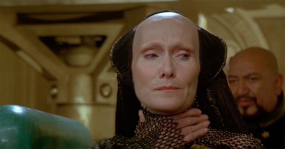 Reverend Mother Gaius Helen Mohiam in Dune 1984 standing near the Emperor in an imperial chamber, composed and observant.