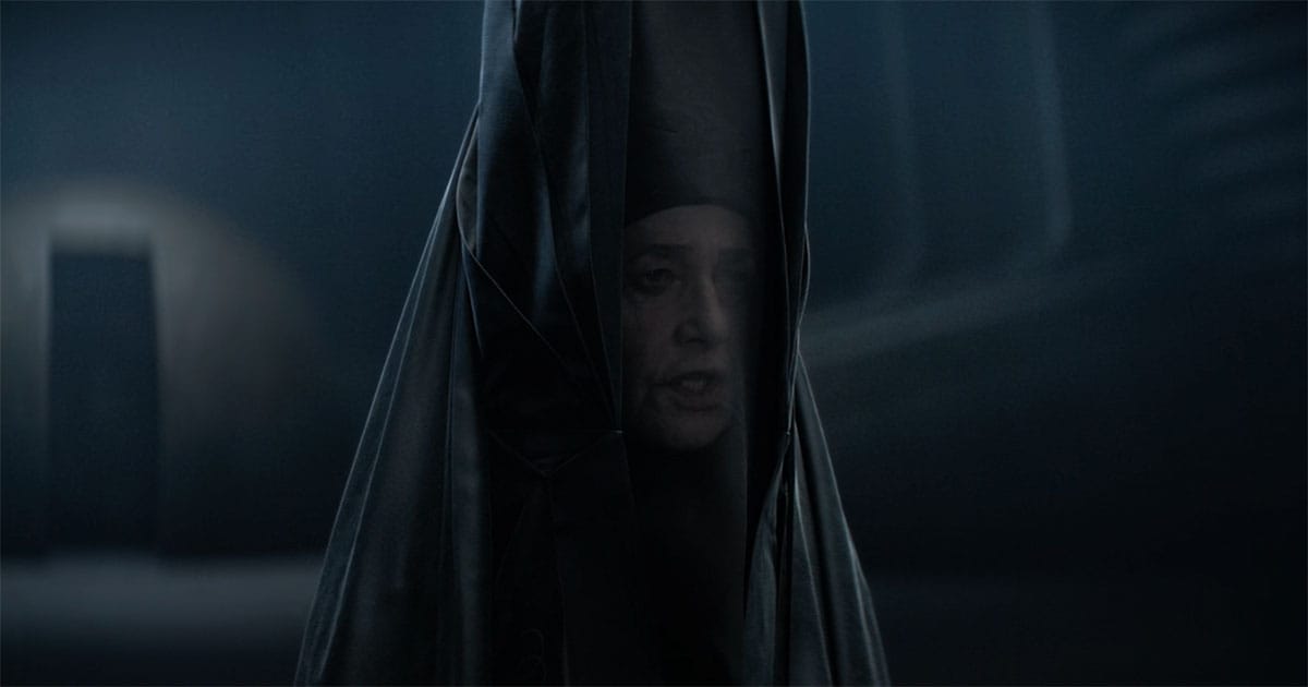 Reverend Mother Gaius Helen Mohiam in Dune 2021, veiled and partially obscured in darkness, standing alone in a dim interior.
