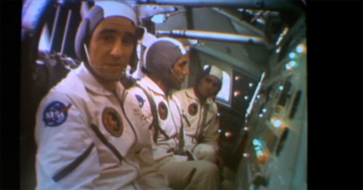 Three astronauts seated inside a spacecraft cabin during a staged broadcast scene from the 1977 science fiction film Capricorn One.