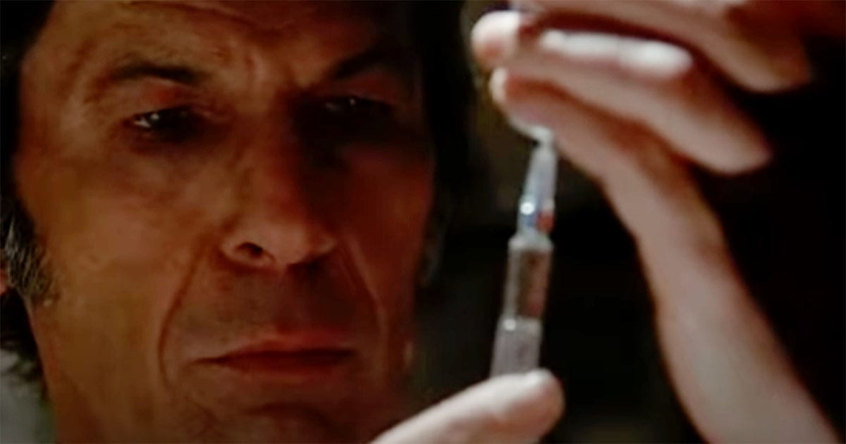 Man in a laboratory setting holding a syringe with calm focus, suggesting clinical authority and controlled procedure in a 1970s science fiction film.