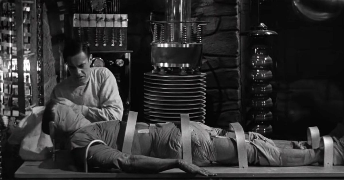 Laboratory scene from the 1931 film Frankenstein showing a restrained body on a table surrounded by early scientific equipment.