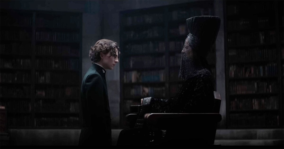 Paul Atreides kneels before a seated Bene Gesserit Reverend Mother in a dim chamber lined with bookshelves.