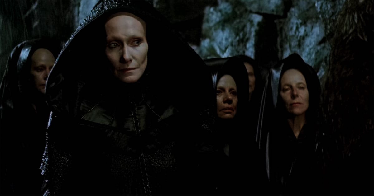 A group of Bene Gesserit Reverend Mothers in black robes stands together in a dim ceremonial setting.