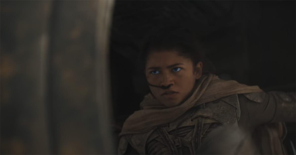 Chani from "Dune" 2021 wearing a stillsuit and scarf, looking alert and tense in low light.