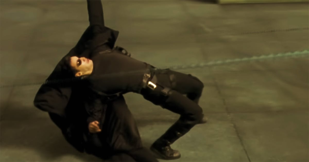 Neo bending backward to evade gunfire inside the simulated world of The Matrix, showing danger and physical reaction before full control is achieved.