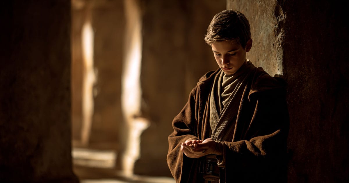 Young Jedi apprentice looking down at hands in temple setting representing internal conflict and understanding of the Force in Star Wars.