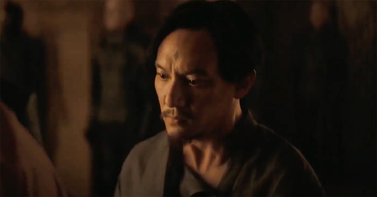 A weary man with a diamond mark on his forehead stands in dim amber light, his expression caught between sorrow and resolve.