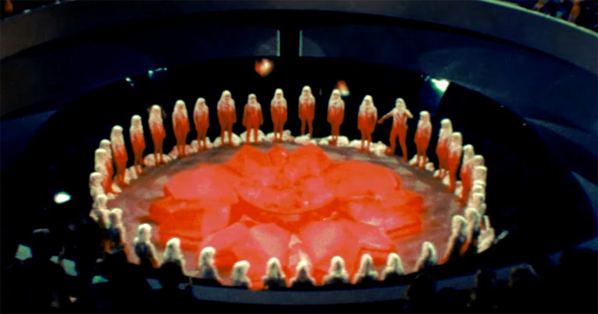 Carrousel ceremony with citizens standing in a circle around the red renewal flower in the 1976 science fiction film Logan’s Run.