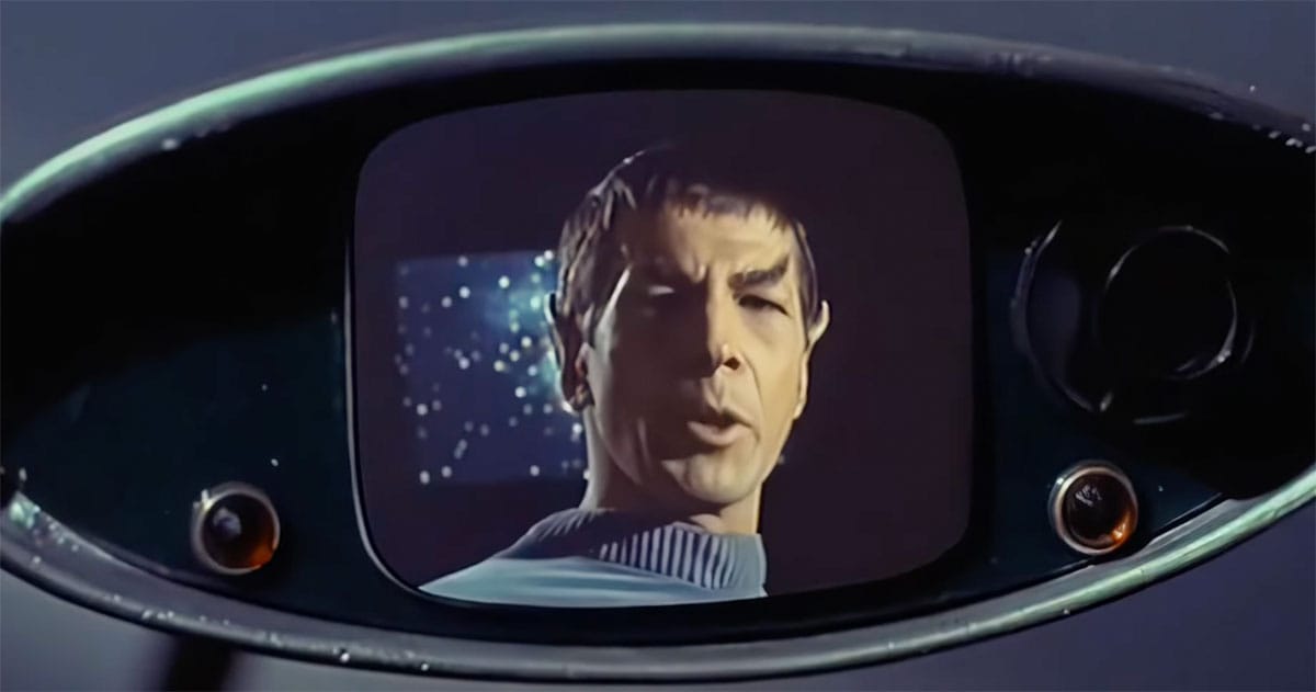 Spock shown on a starship viewscreen during a video communication in Star Trek, his calm expression framed by the curved display against a starfield.