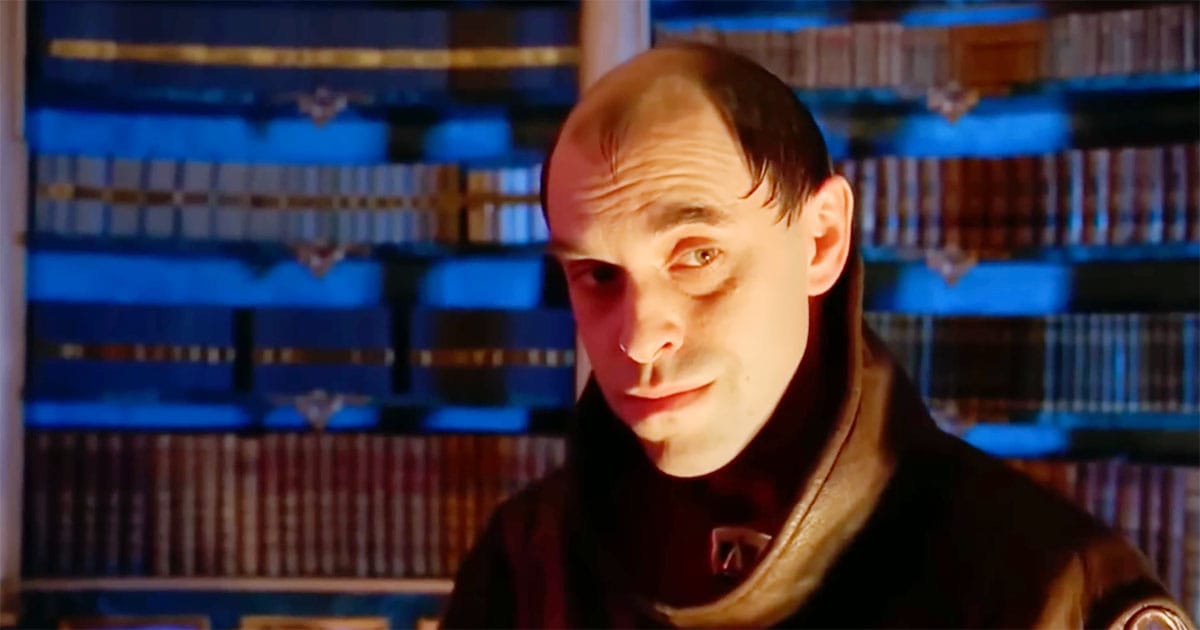 A reserved imperial court figure with a pale, watchful expression, standing before rows of records in a dimly lit interior.