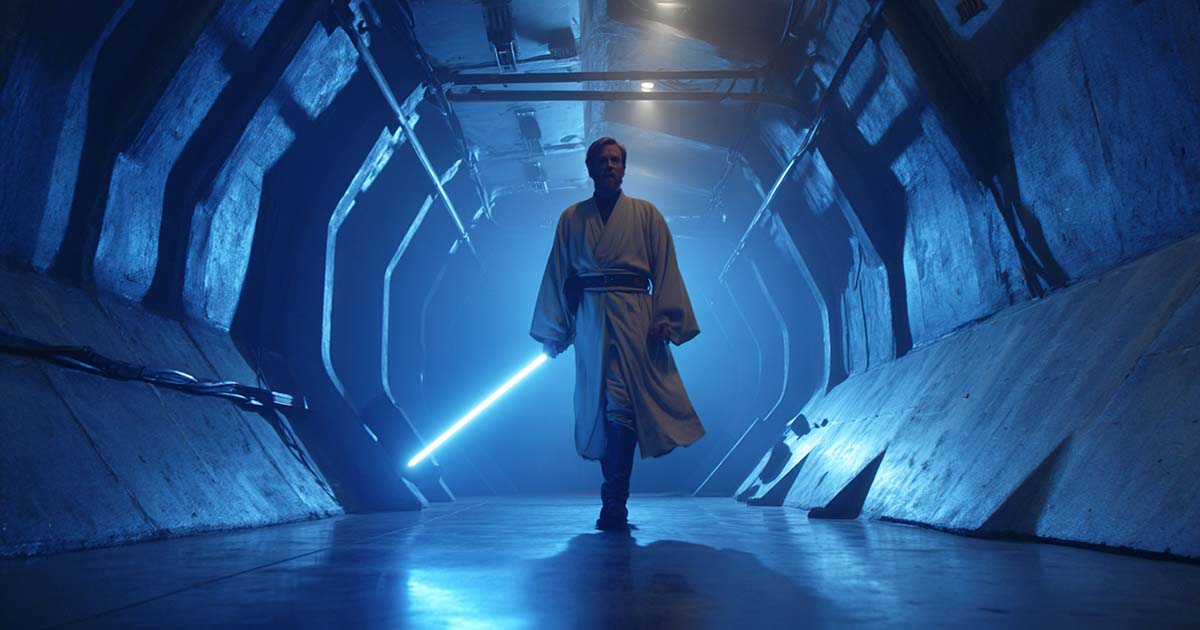 Obi-Wan Kenobi holding a glowing blue lightsaber in a metallic Death Star hallway in "Star Wars" (1977).